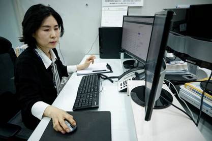 A woman in a white collared shirt and black jacket works at a computer.
